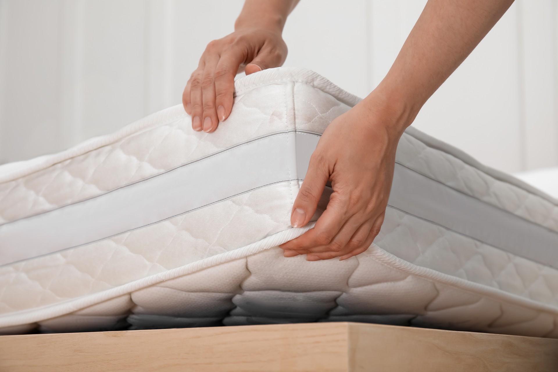 Mujer poniendo colchón blanco suave en la cama en el interior, primer plano