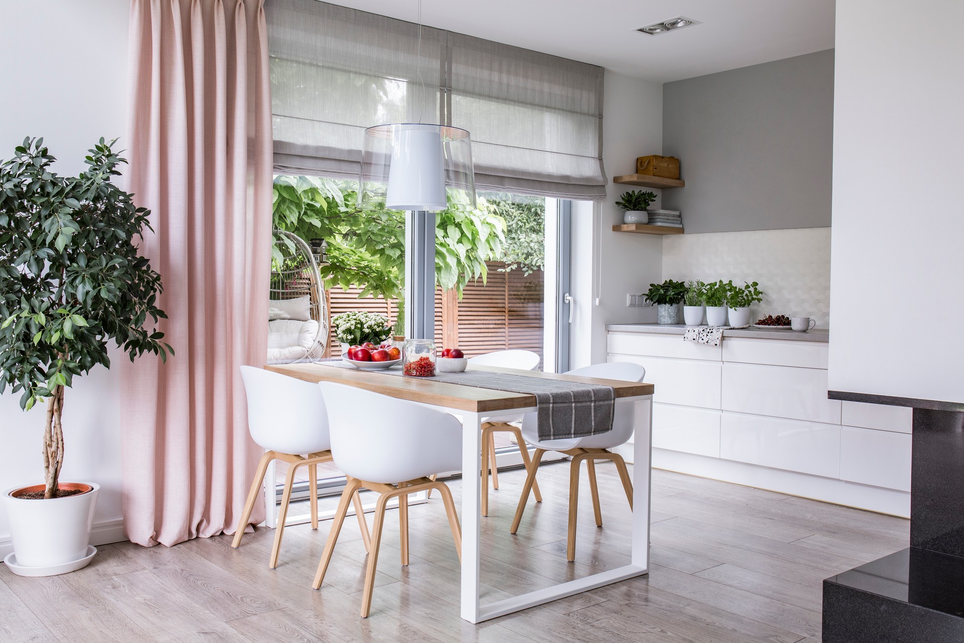 Cortinas romanas de gris y una cortina rosa en grande, ventanas de vidrio en una moderna cocina y comedor interior con una mesa de madera y sillas blancas